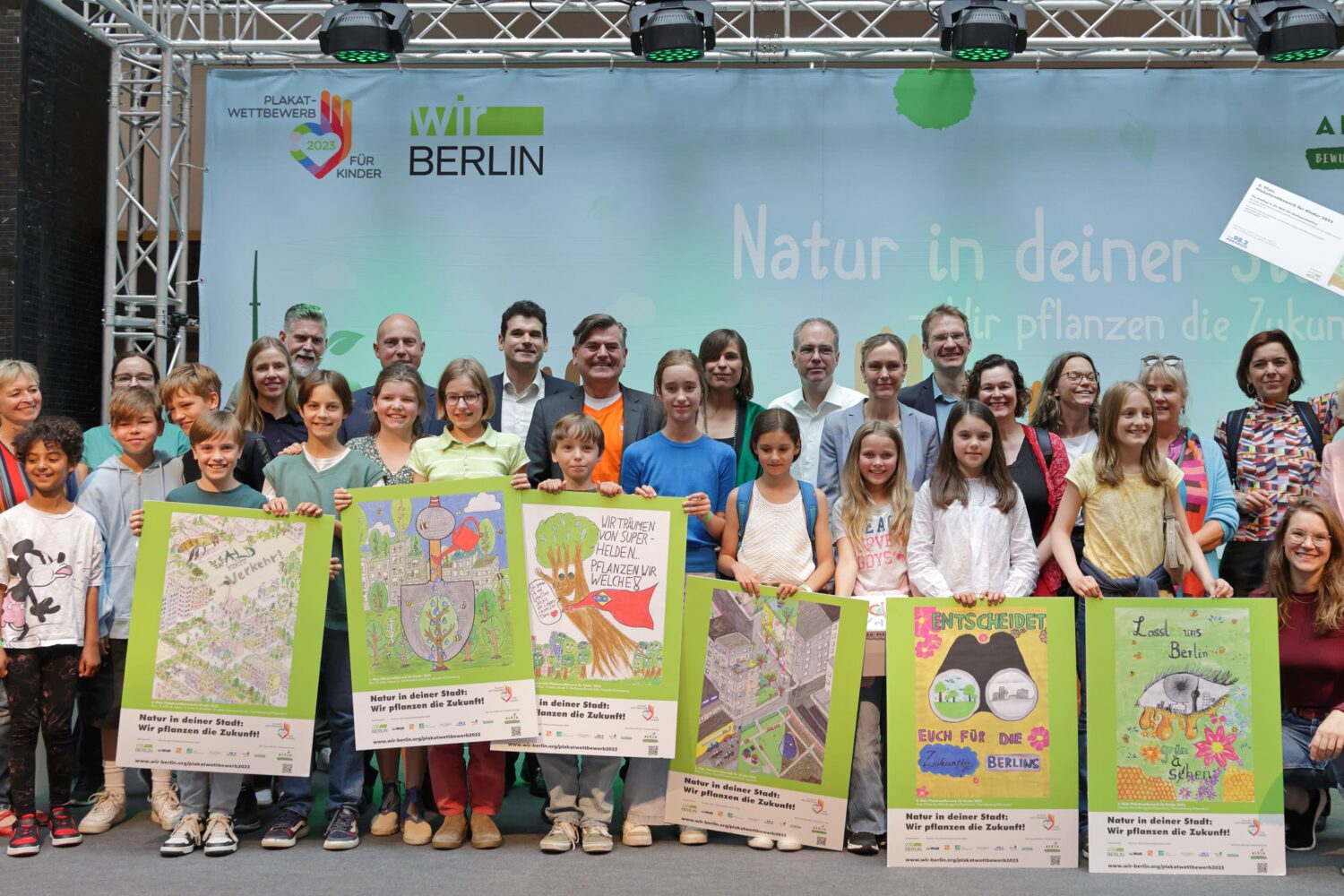 Auf einer „große Bühne“ im ALEXA Shopping wurden die Gewinner des Berlin weiten Plakatwettbewersb der Initiative wirBerlin zum Thema „Natur in der deiner Stadt“ gekürt. In der vorderen Reihe sind Kinder mit ihren Plakaten zu sehen, dahinter Personen aus dem Event-Team, Centermanagement, Partnerunternehmen, Medien und berliner Senat.
