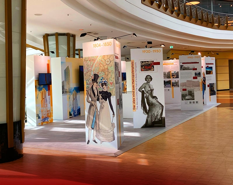 Im Innenraum des ALEXA Shopping Centers findet die Ausstellung „ZUKUNFT ALEXANDERPLATZ. EIN PLATZ im WANDEL.“ statt. Zu sehen sind dreieckige Stellwände mit historischen Figuren und Fotos vom Alexanderplatz, dahinter rechteckige Stellwände mit integrierten Bildschirmen, auf welchen Videos über die Gegenwart und Zukunft vom Alexanderplatz informiert wird.