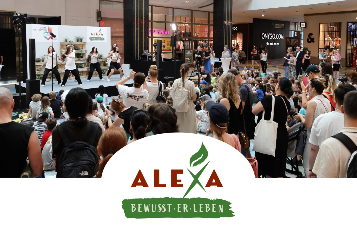 Im ALEXA Shoppingcenter fand das Event „Bewusst(er)leben 2022“ statt. Auf dem Bild wird den Teilnehmern und Besuchern ein Bühnenprogramm mit Entertainment zu Umweltthemen geboten. Unter dem Bild ist das Logo des Events „Bewusst(er)leben 2022“ platziert.