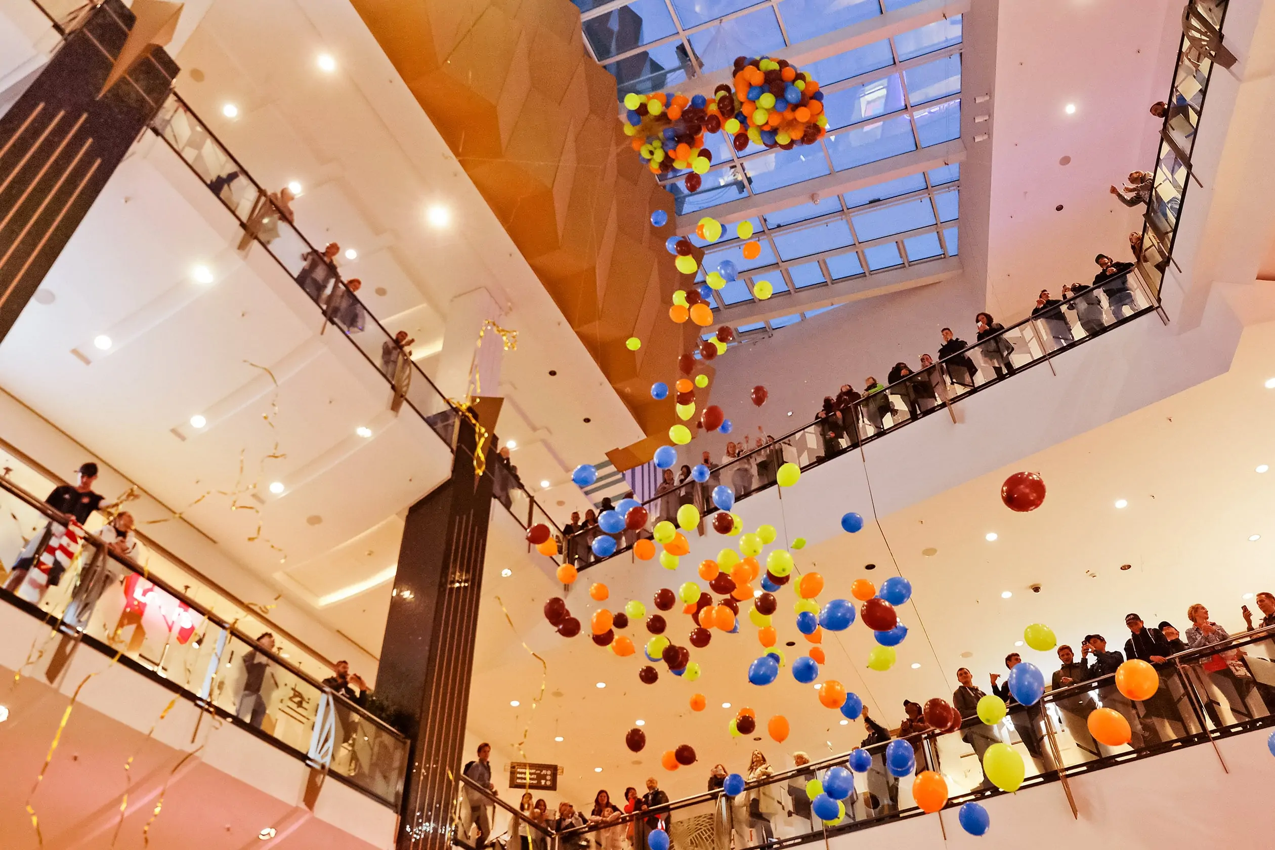 Ein Ballon-Regen fällt von der Decke des Innenraums vom ALEXA Shoppingcenter herunter. Zahlreiche Besucher der Show im Rahmen des Events ALEXA NEW COLOURS OF SHOPPING schauen von den Rängen den fallenden Ballons zu.