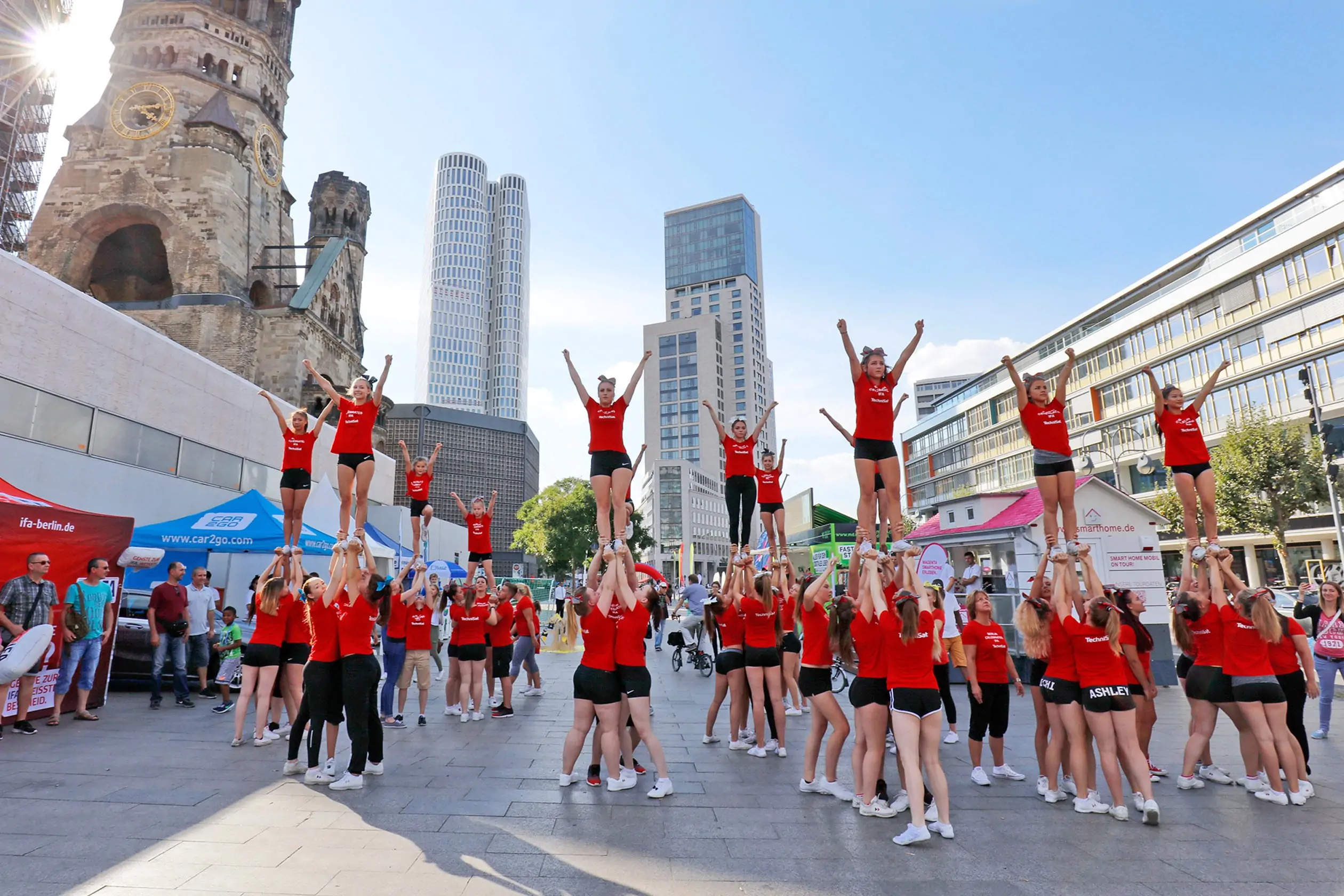 Eine Aufnahme einer Akrobatikshow auf dem Breitscheidplatz in Berlin, auf dem das Event Berlin Celebrates IFA stattfindet. Eine Gruppe von circa 60 Mädchen bilden kleine Gruppen. aus jeder Gruppe wird ein Mädchen senkrecht nach oben gestemmt. So entstehen mehrere menschliche Pyramiden. Zahlreiche Zuschauer verfolgen die Show. Trendshow Kurfürstendamm City West