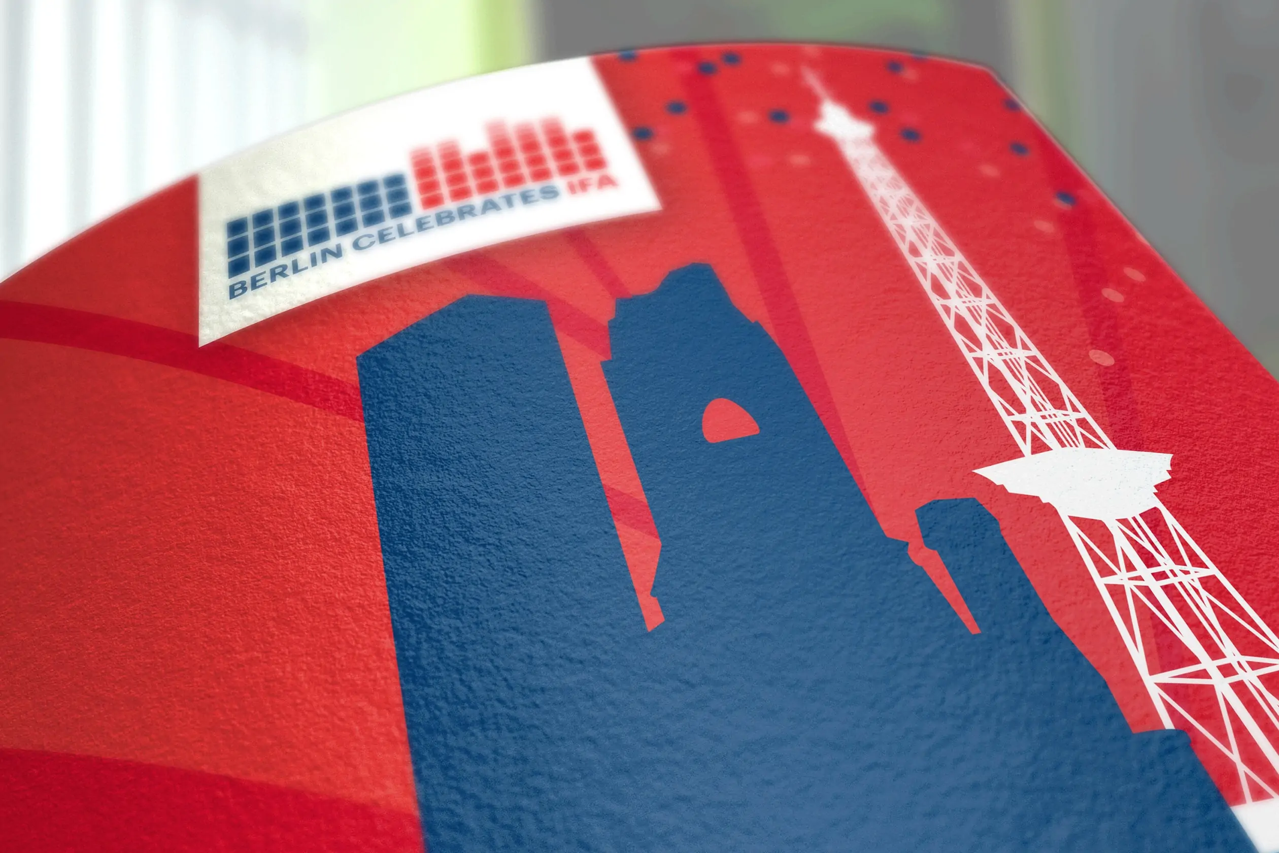 Das Key Visual des Events Berlin Celebrates IFA, bestehend aus dunkelblauer Silhouette der Gedächtniskirche und weisser Silhouette des Funkturms auf rotem Hintergrund. Darüber ist das Logo von Berlin Celebrates IFA zu sehen. Beide Elemente sind eine Kreation von AD AGENDA. Trendshow Kurfürstendamm City West Breitscheidplatz